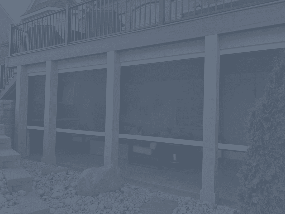 Angled view of an upper deck with dark railing above a covered lower patio area enclosed by motorized retractable screens, adjacent to stone steps and rock landscaping.